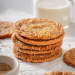 A stack of sesame cookies on parchment paper with milk nearby.