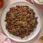 A top down view of a plate of Korean beef bulgogi surrounded by table settings.