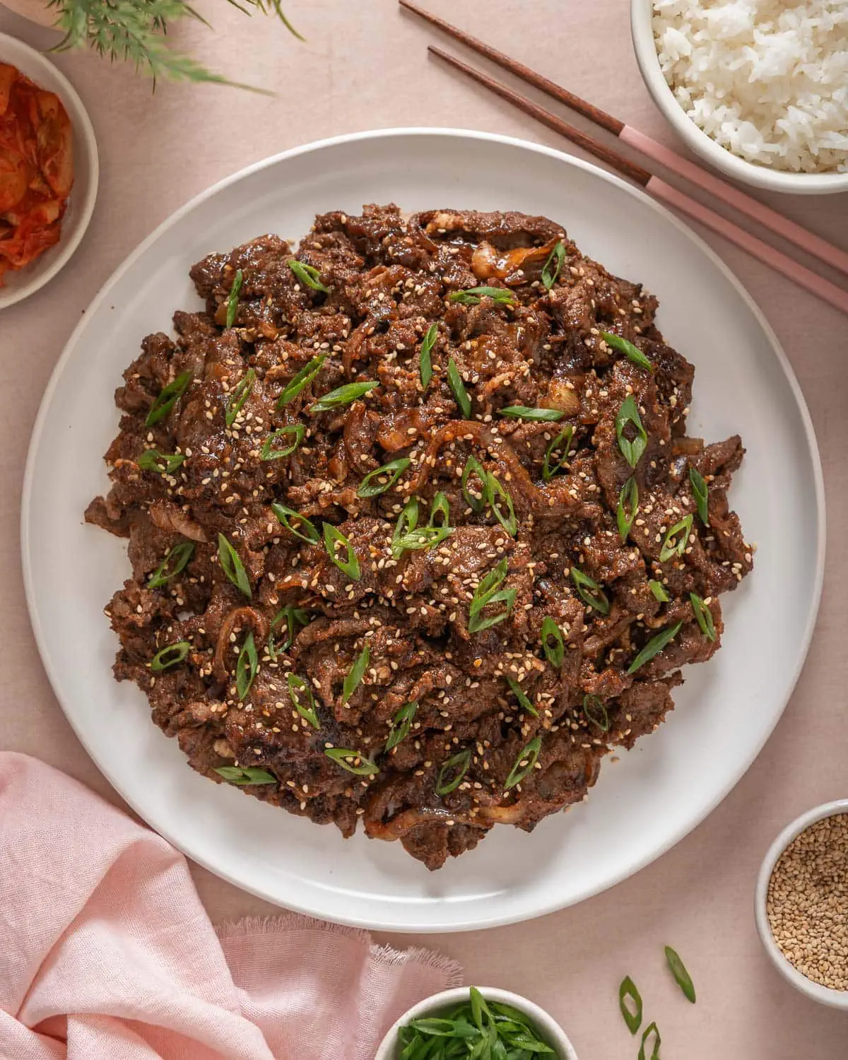 A top down view of a plate of Korean beef bulgogi surrounded by table settings.