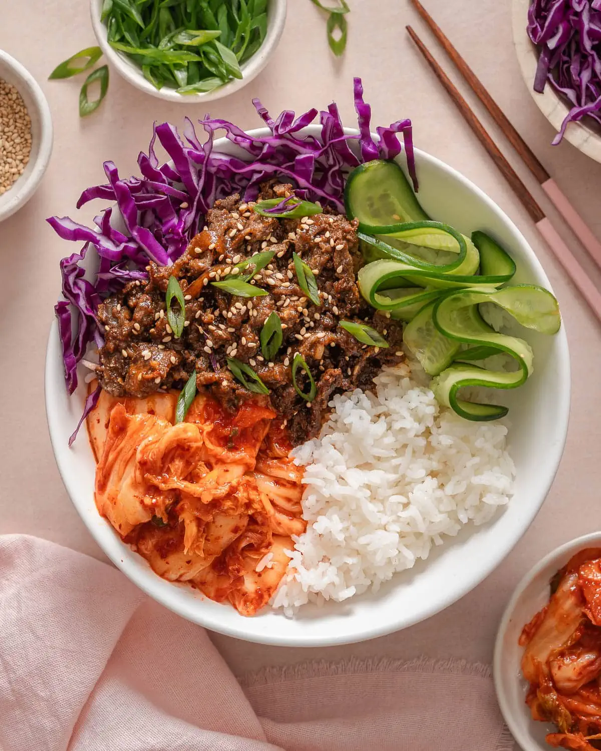 A top down view of a bulgogi bowl with various vegetable sides, kimchi, and rice.