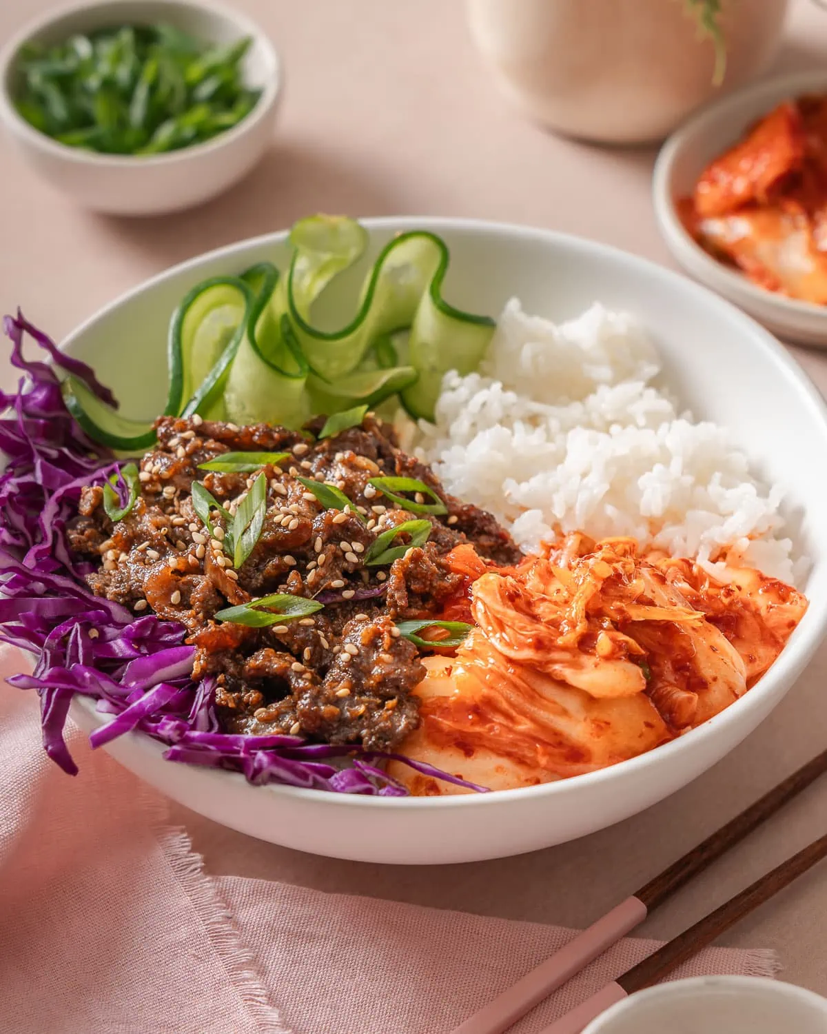 A bulgogi bowl on a table featuring beef bulgogi, kimchi, vegetables, and rice.