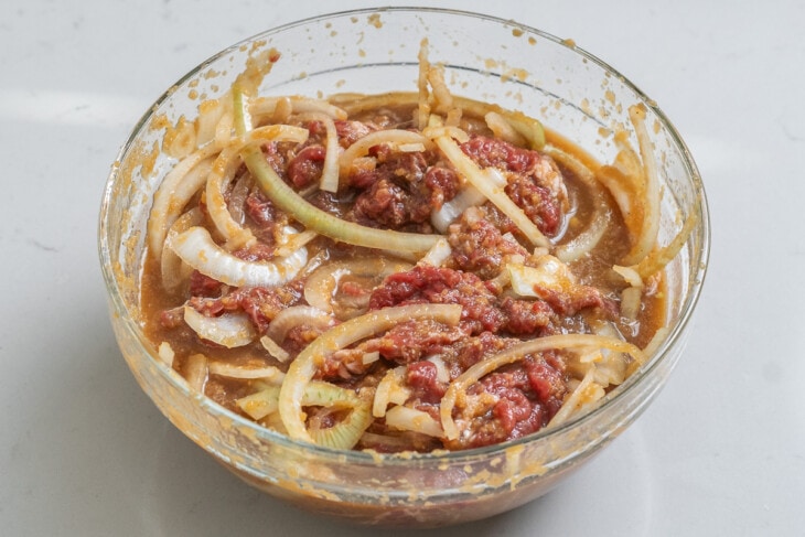 Thin sliced beef and onion tossed with a marinating in sauce inside a large glass bowl.