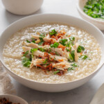 A bowl of chao ga on a table garnished with green onion and fried shallots.