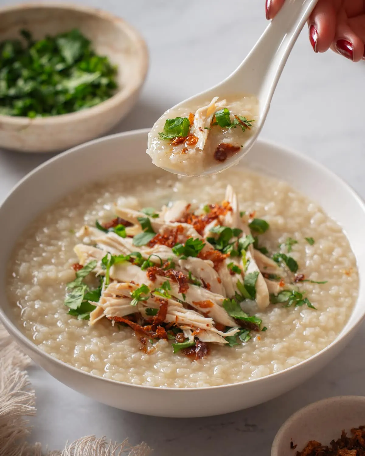 A spoon of chicken rice porridge being lifted from a bowl of chao ga.