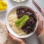 Someone setting down a a bowl of Jajangmyeon on a table.