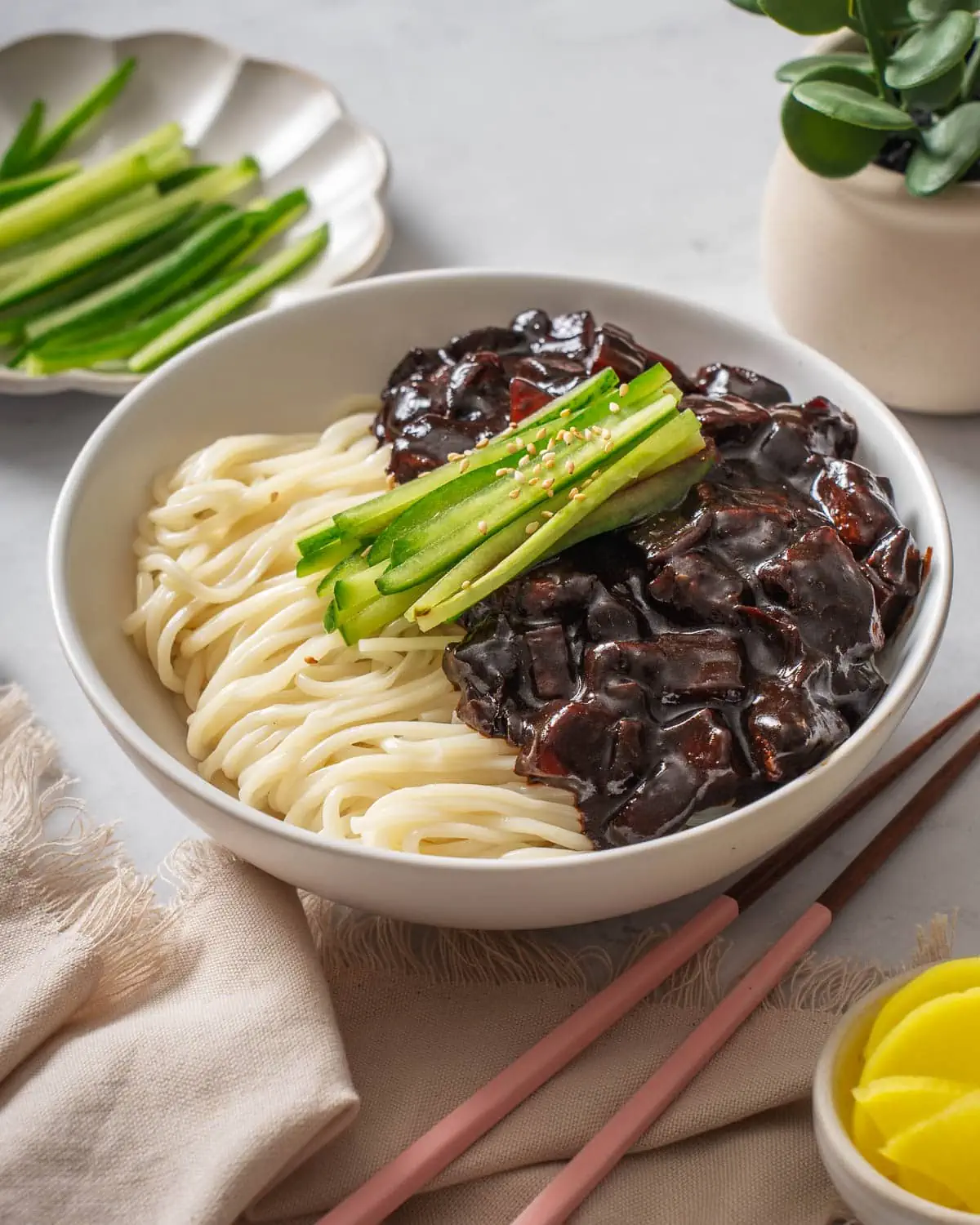 A bowl of Korean black bean noodles on a table with table settings surrounding it.