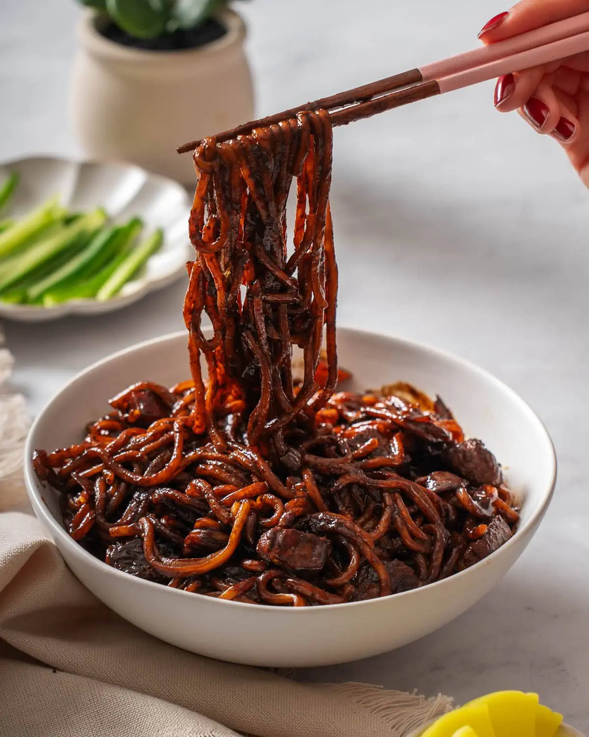 Lifting up noodles from a bowl of Korean black bean noodles.