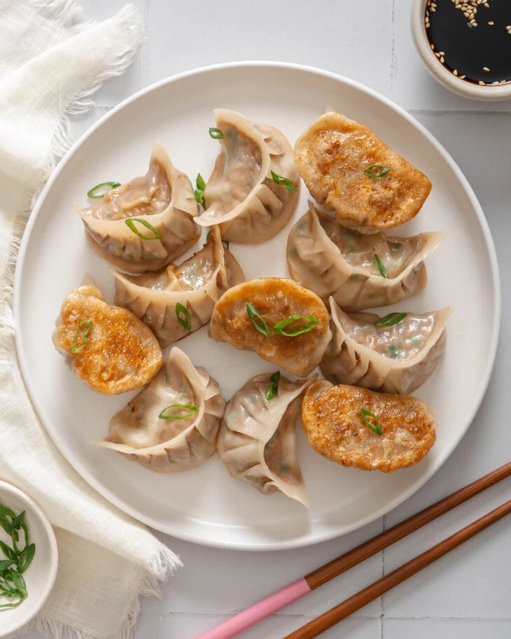 A top down view of a plate of pan fried pork and chive dumplings surrounded by table settings.