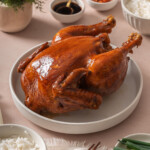 A whole soy sauce chicken on a platter surrounded by table settings.