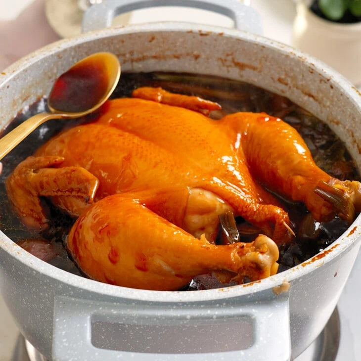 A whole chicken being basted and cooked in a soy sauce based sauce.