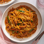 A top down view of chicken lo mein on a plate surrounded by table settings.