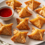 A plate of crab rangoons with a small bowl of sweet chili sauce.
