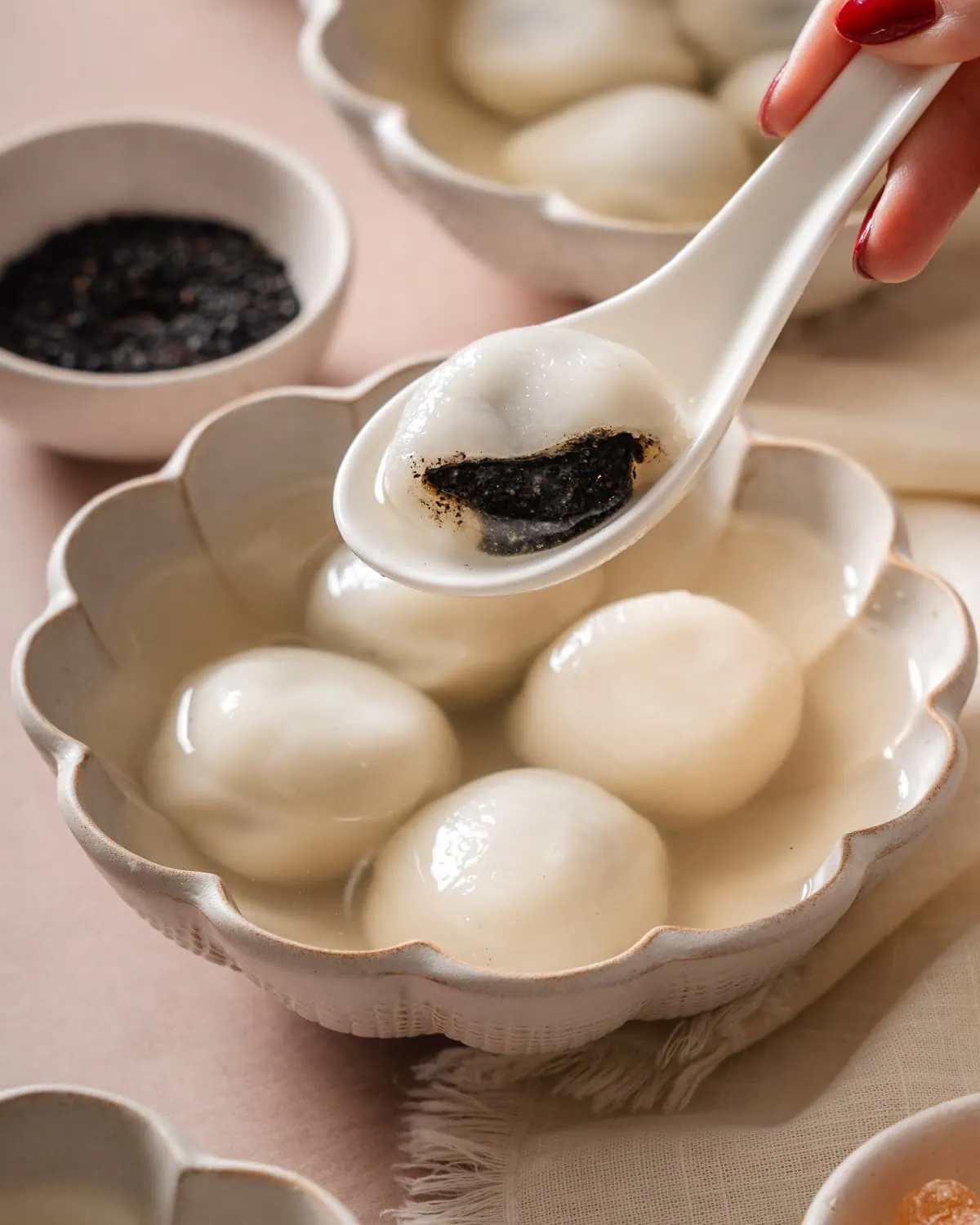 A spoon holding up a bit open tang yuan over a bowl of more tang yuan.