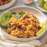 A plate of Thai basil fried rice served with sliced cucumbers and lime slices.