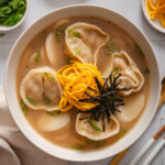 A top down view of tteok mandu guk surrounded by table settings.