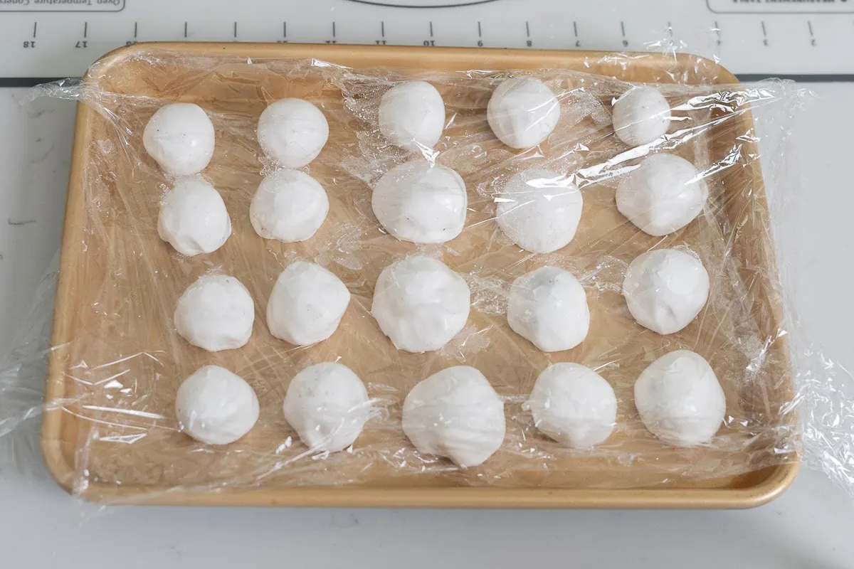 Balls of dough on a plastic wrap covered tray.