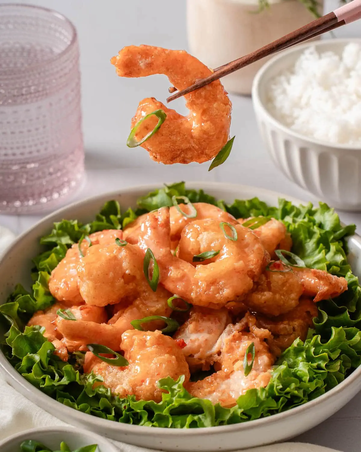 A pair of chopsticks holding up a bang bang shrimp.