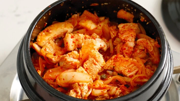 Pork belly, kimchi, and mushrooms cooking in a stone pot.