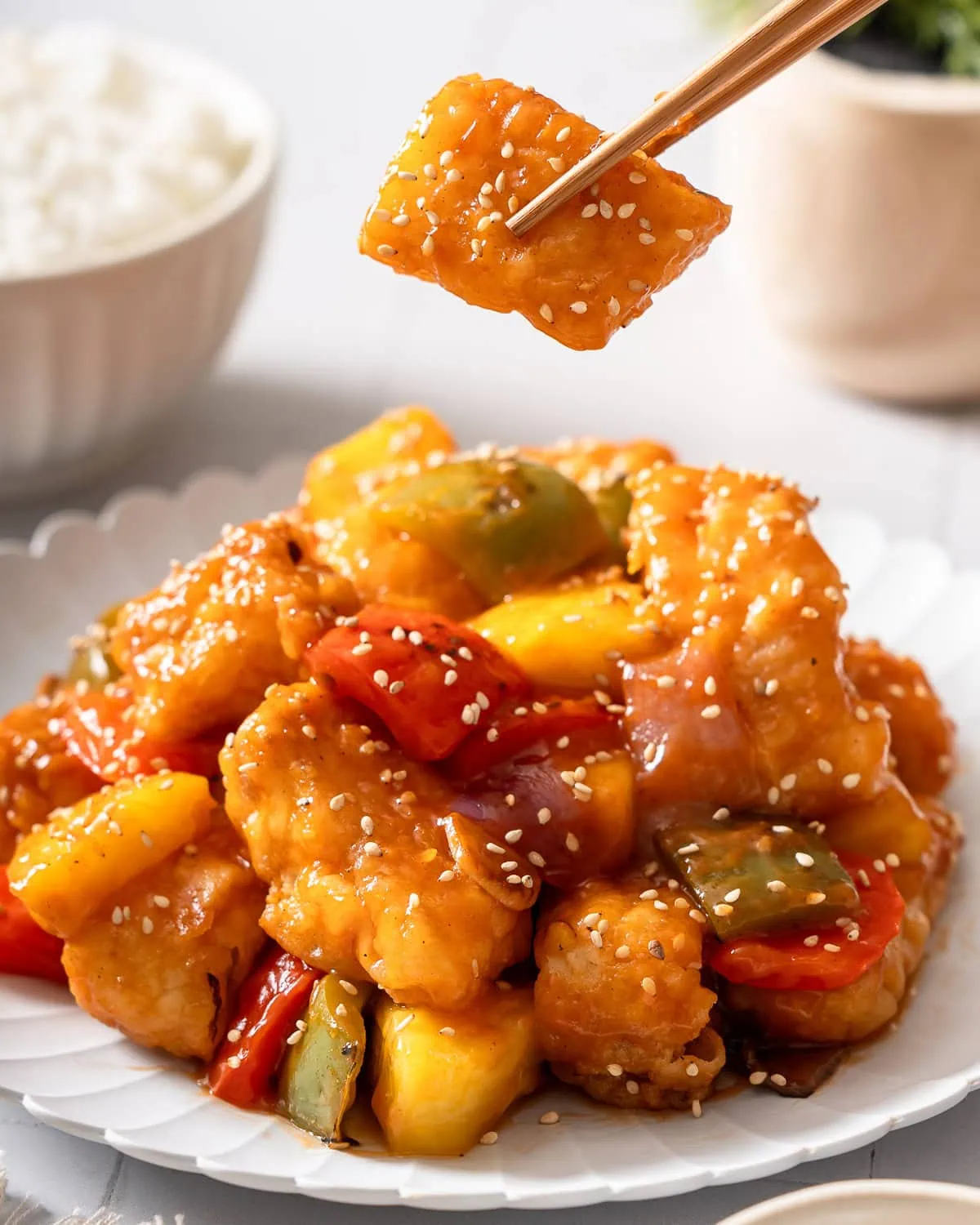 A pair of chopsticks lifting up a piece of sweet and sour fish.