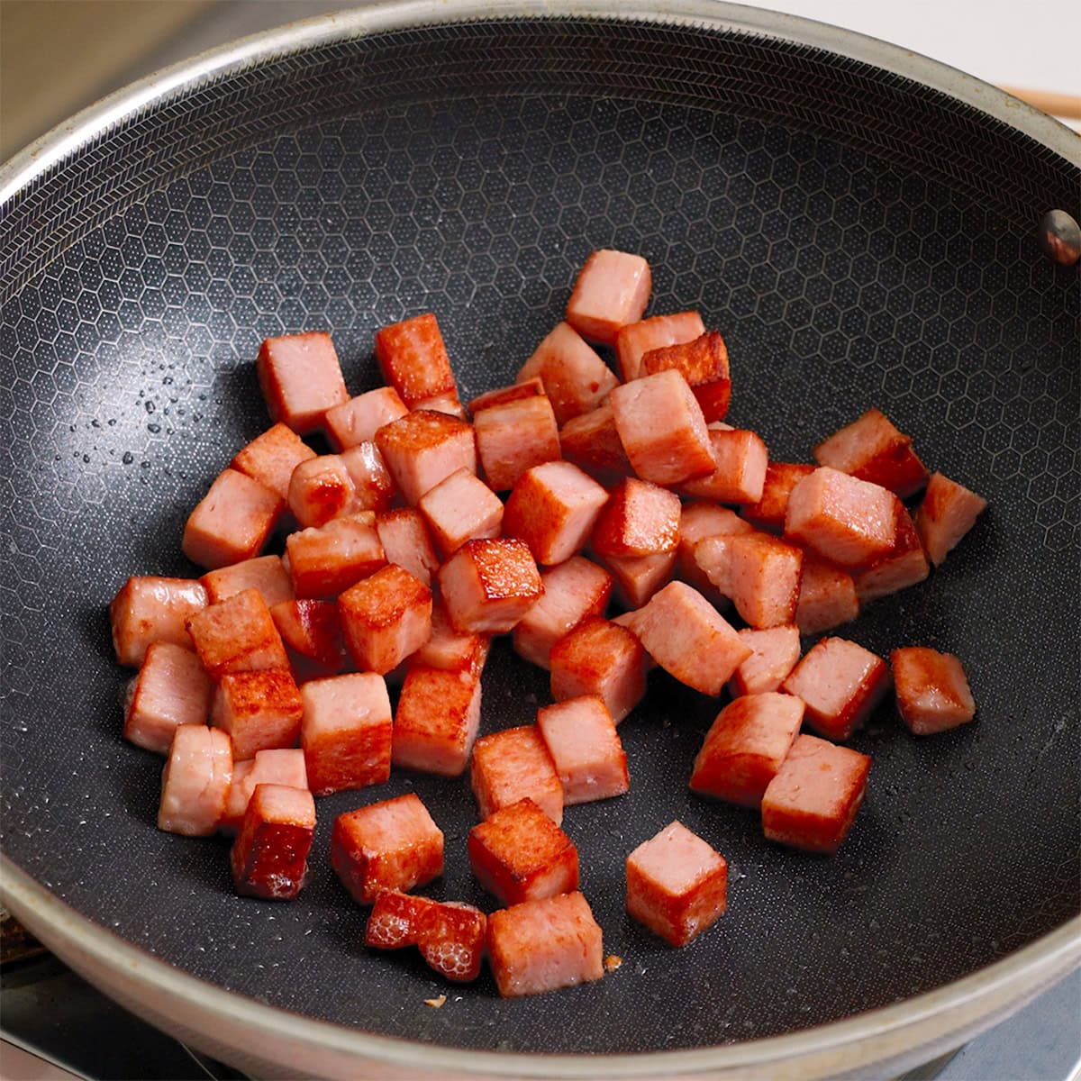 Cubed spam cooking in a large wok.