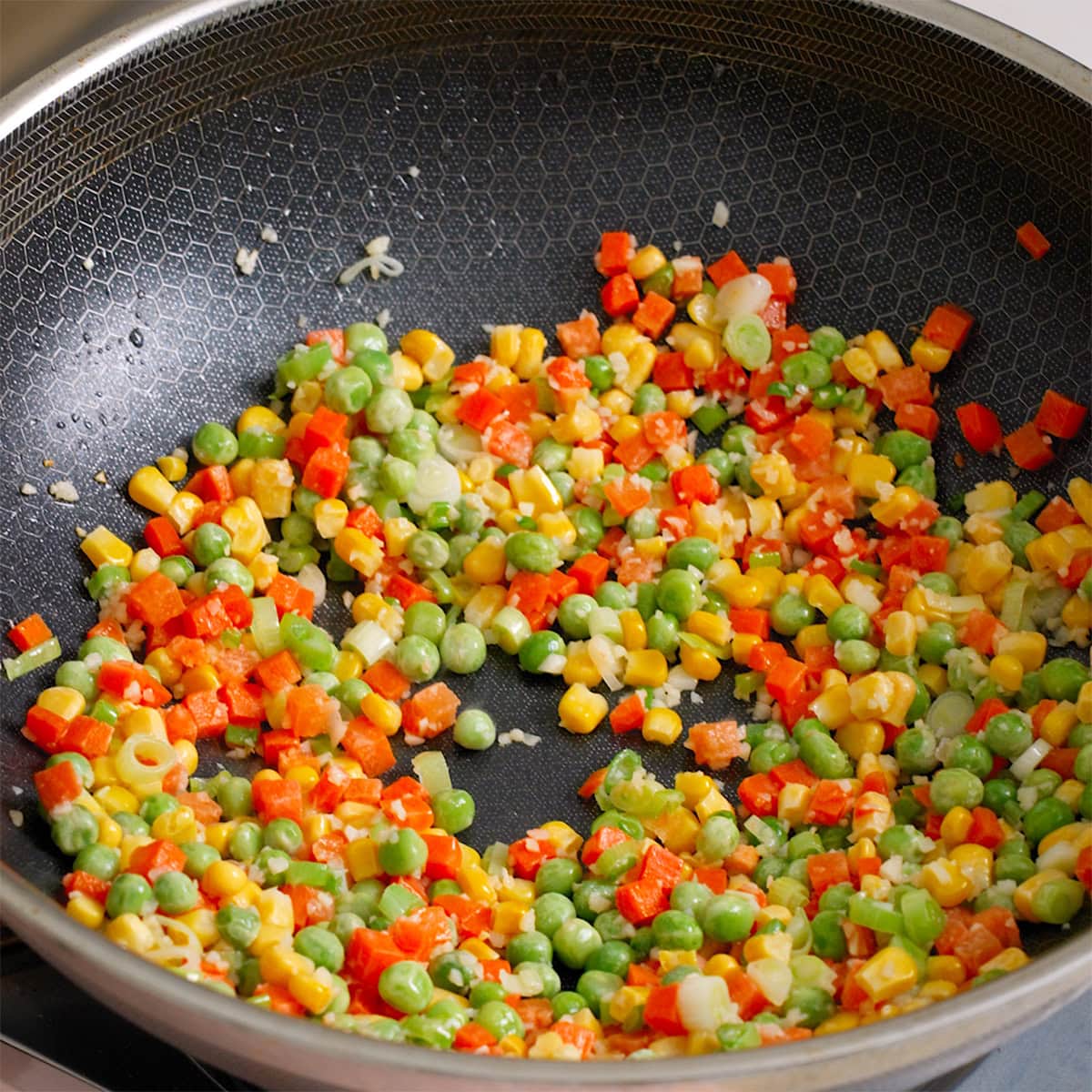 Frozen vegetables and aromatics cooking a wok.