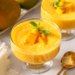 Two dessert glasses full of mango sago with fresh mangos nearby.
