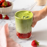 A hand grabbing a strawberry matcha latte with a straw in it.