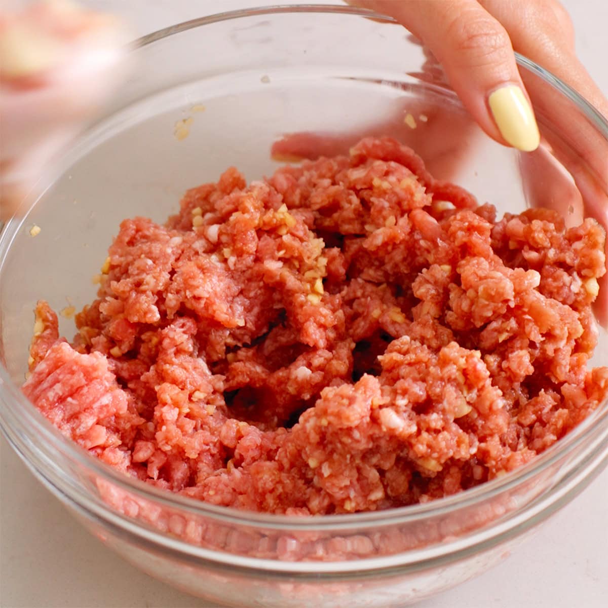Ground pork tossed with a marinade in small bowl.