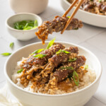 A pair of chopsticks holding up a beef enoki roll.