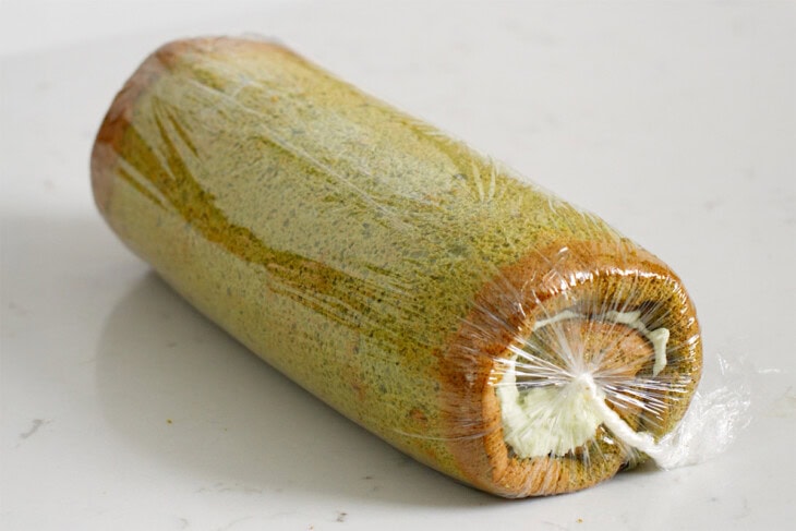 A matcha cake roll wrapped in plastic to chill.