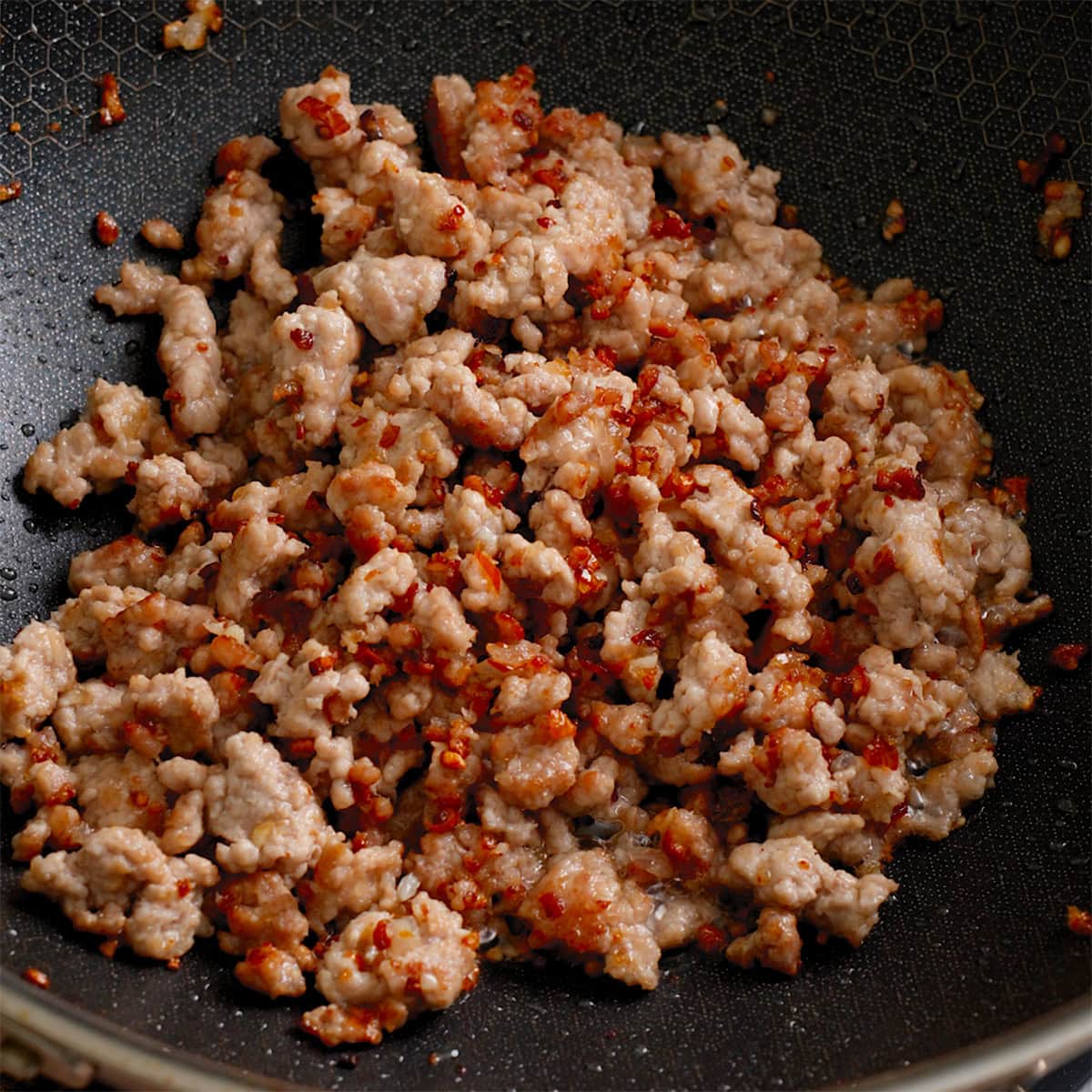 Ground pork tossed with aromatics in a wok.