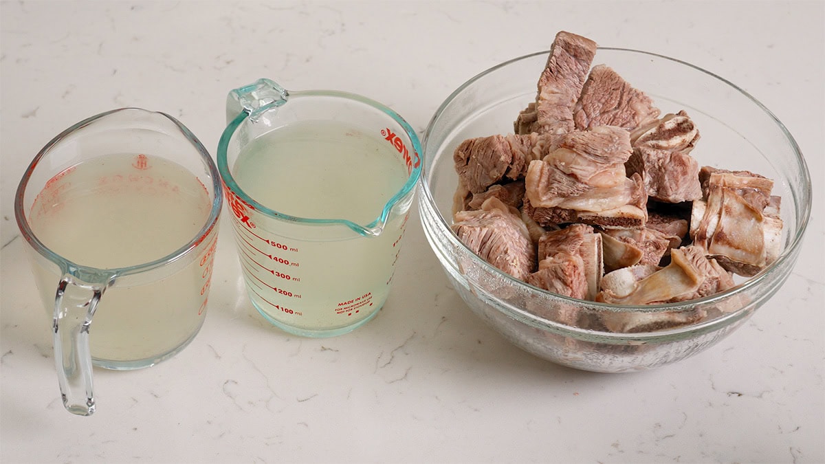 Poached beef short ribs and beef stock in containers.