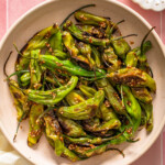 A plate of blistered shishito peppers tossed in sauce.