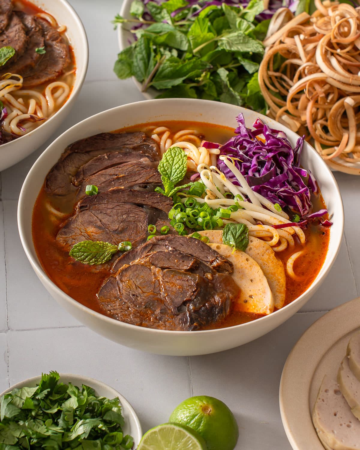 A bowl of bun bo hue surrounded by garnishes.