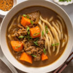 A bowl of Japanese curry udon surrounded by table settings.