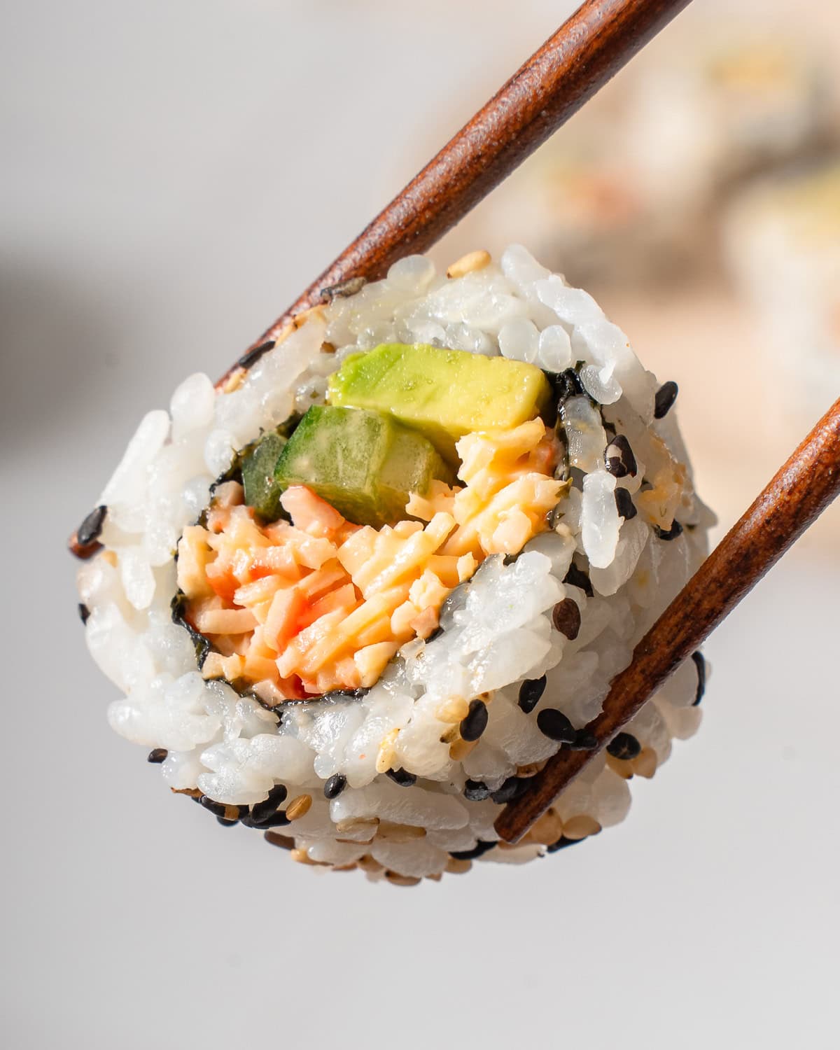 A kani sushi bite held up by a pair of chopsticks.