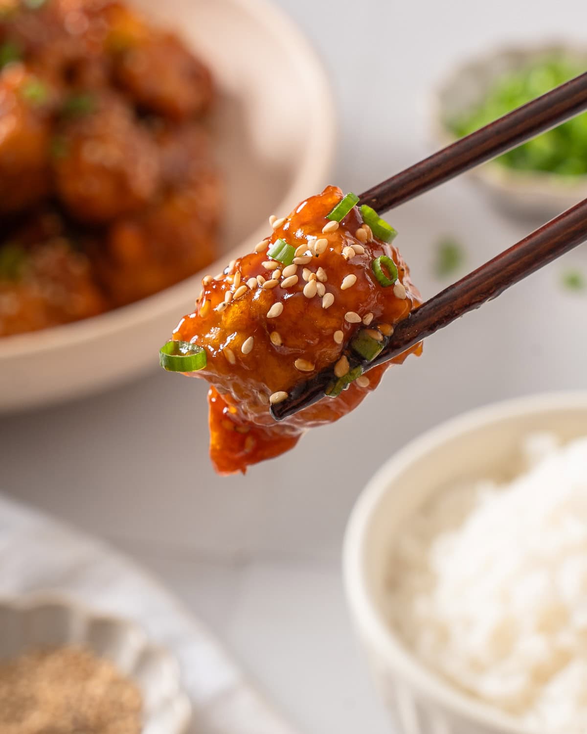 A piece of honey sesame chicken held up by a pair of chopsticks.