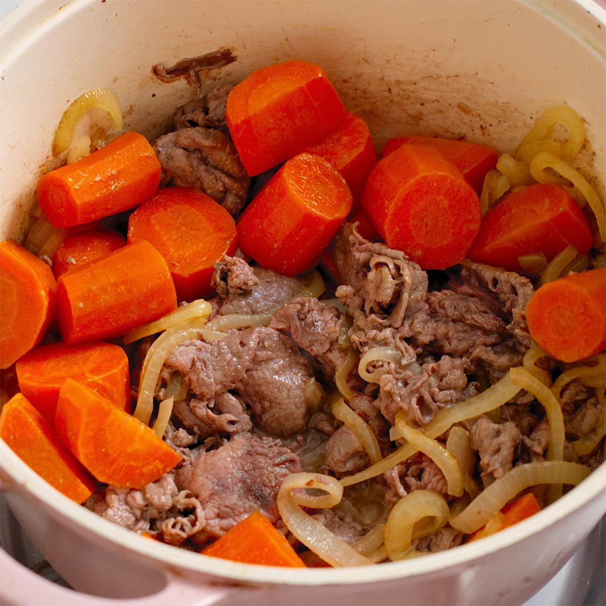 Carrots, onions, and sliced beef cooked in a large stock pot.