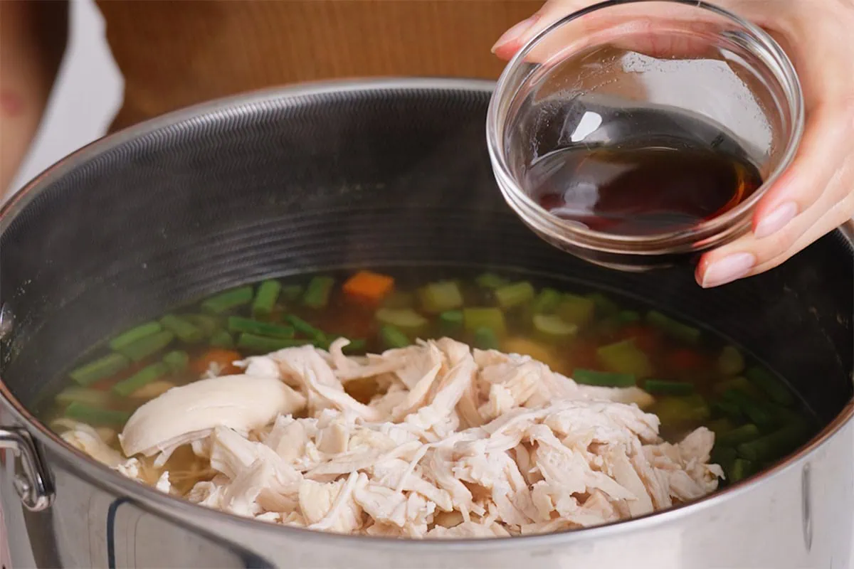 Adding fish sauce to a pot of Vietnamese chicken noodle soup.