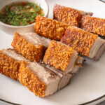 Slices of crispy pork belly on a plate with a side of dipping sauce.