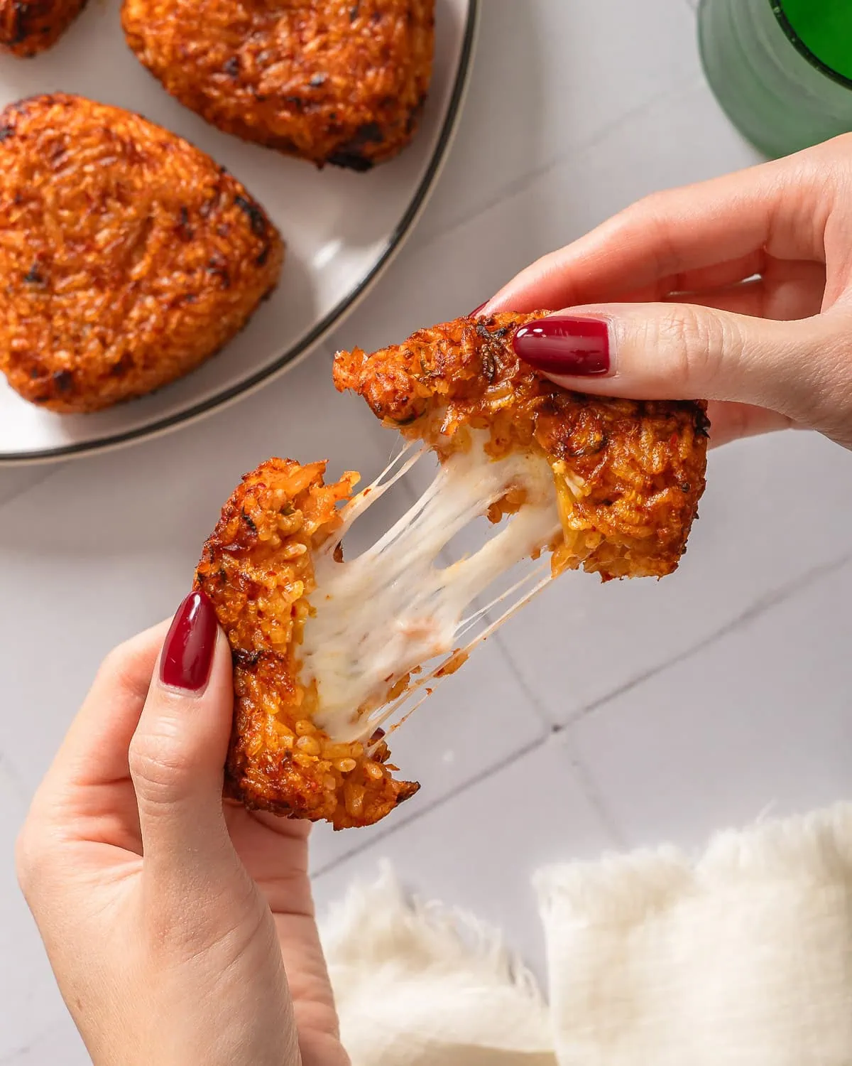 Hand pulling apart a cheesy kimchi rice ball to show the cheese stretching.