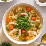 A bowl of Vietnamese chicken noodle soup garnished and surrounded by table settings.