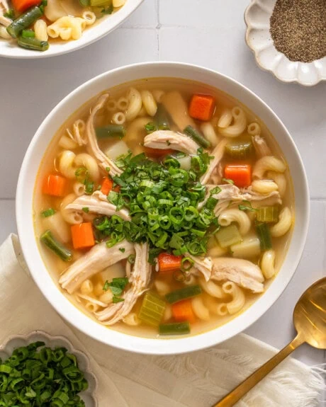 A bowl of Vietnamese chicken noodle soup garnished and surrounded by table settings.