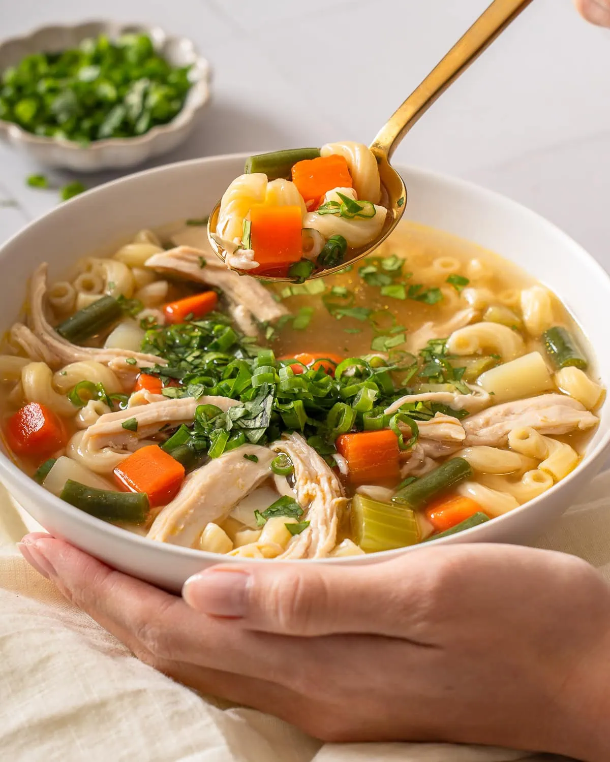 A spoonful of Vietnamese chicken noodle soup being lifted up from a bowl.