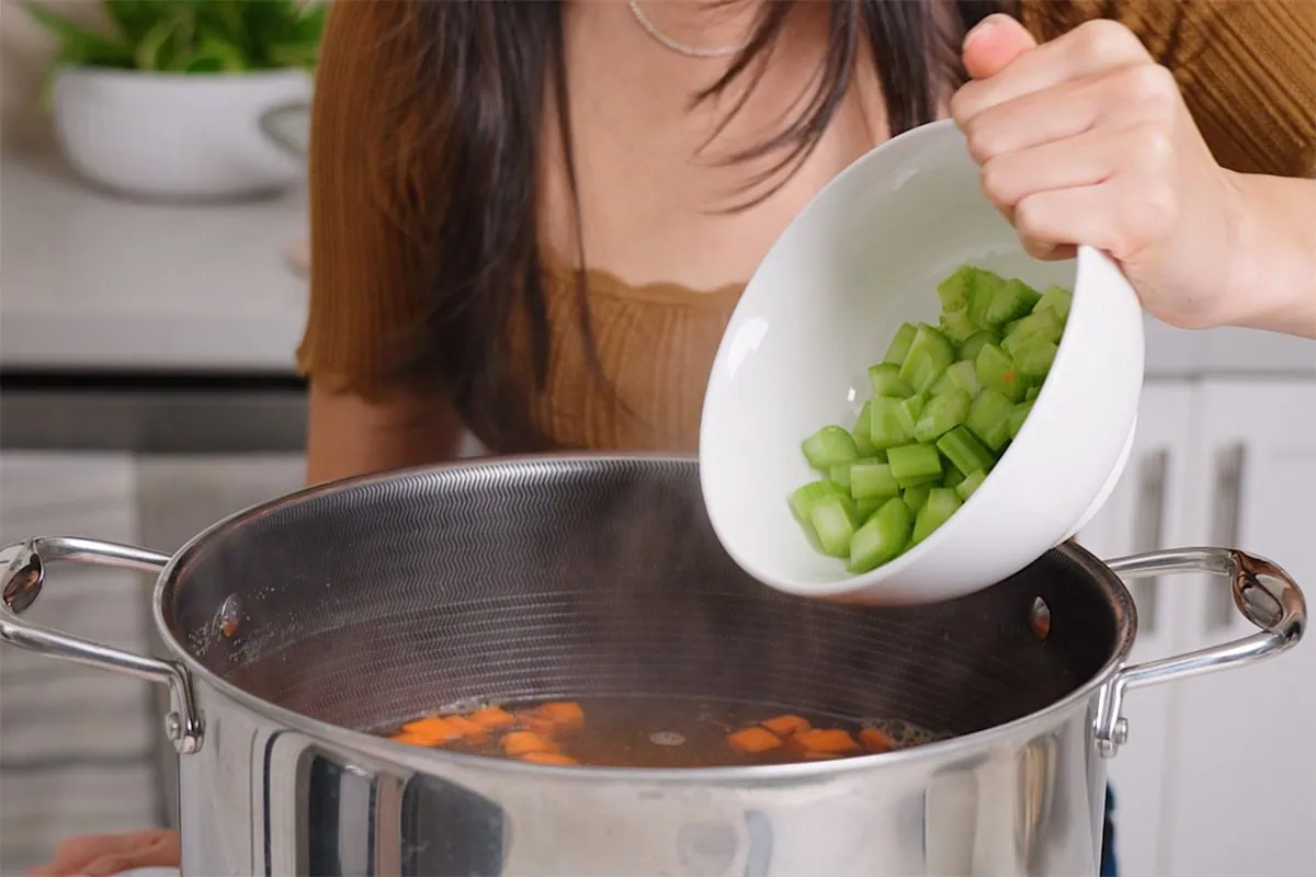 Adding diced celery and carrots to a pot of soup.