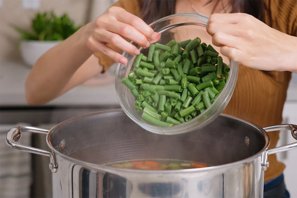 Adding green beans to a pot of soup.