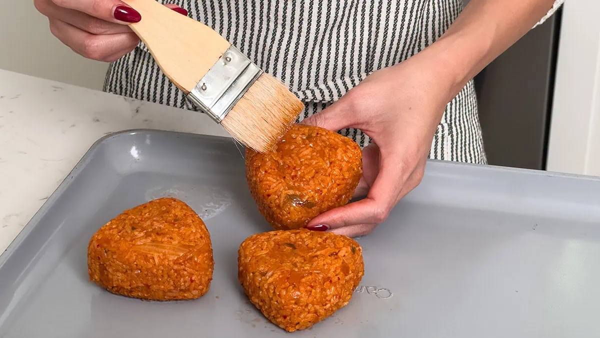 Brushing kimchi rice balls with sesame oil before air frying.