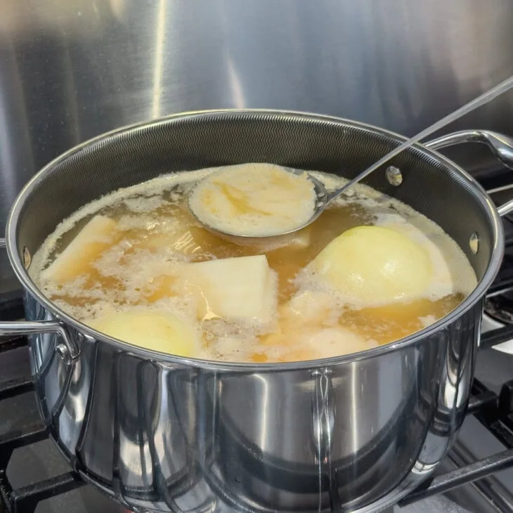 Skimming the top of a pot of chicken broth to clean the broth.