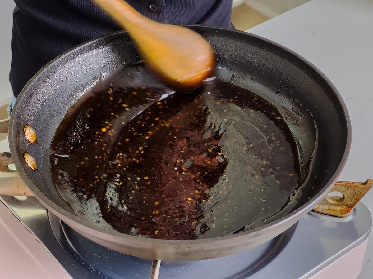 Stirring thickened teriyaki sauce in a large skillet.