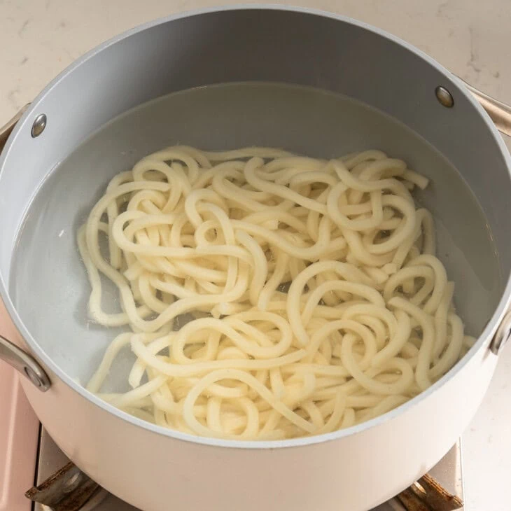 Loosening up udon noodles in a pot of boiling water.